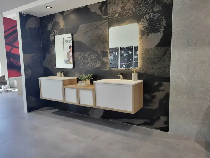 Modern bathroom vanity showroom display featuring multiple double-sink configurations with oak wood and white lacquer cabinetry, wall-mounted mirrors, and decorative tile accent wall