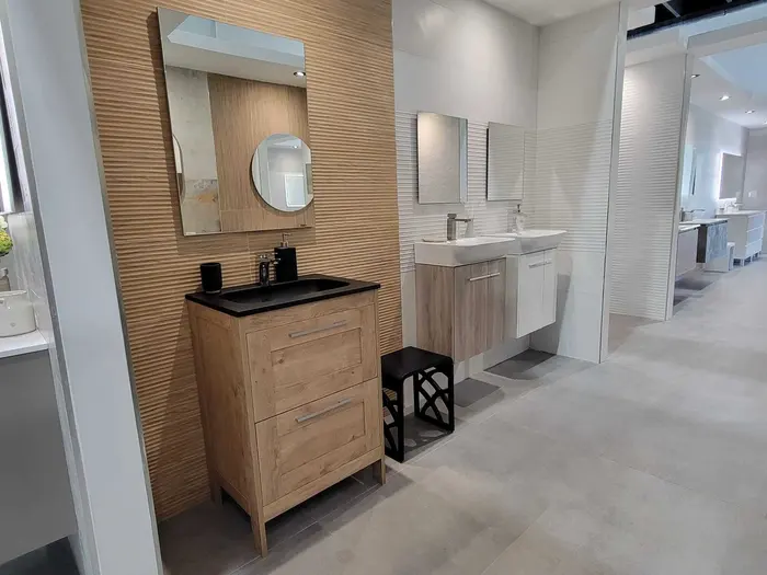 Multiple bathroom vanity display setups in a showroom with wood-look and white textured tile backsplashes