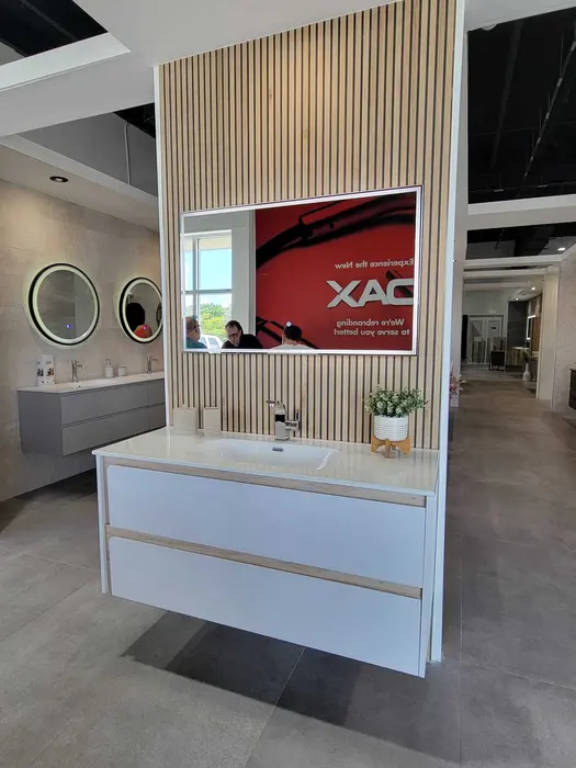 Modern bathroom vanity showroom display featuring white floating vanities, integrated mirrors with LED lighting, vertical slat wall treatment, and tile samples