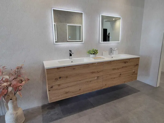 Completed modern bathroom vanity with dual sinks, white composite countertop, warm wood cabinetry, patterned wall tile, and LED-lit mirrors