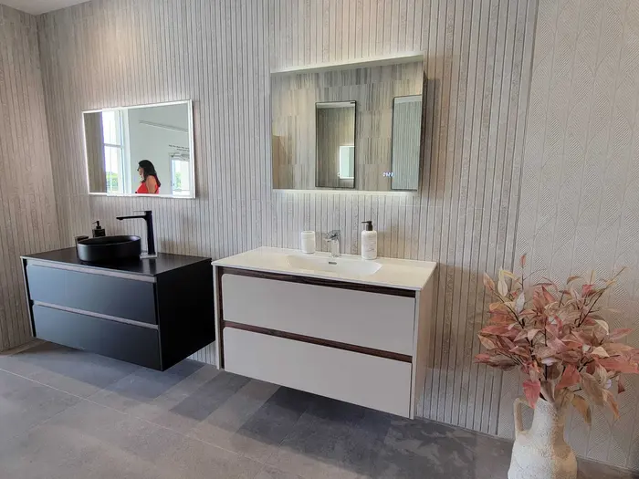 Completed master bathroom with dual black and white floating vanities, LED-lit mirrors, vertical wood-look tile walls, and finished flooring.