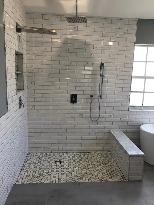 Completed modern bathroom shower with light gray subway tile surround, geometric hexagon floor tile, rainfall showerhead, and black fixtures