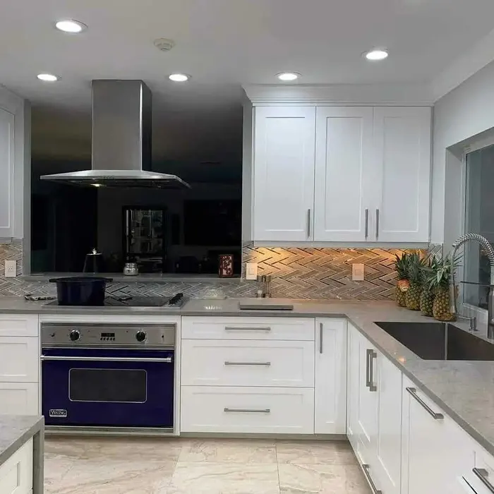 Modern kitchen with white shaker cabinets, black range hood, navy blue oven, geometric herringbone tile backsplash, recessed lighting, and gray quartz countertops