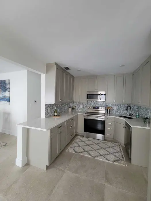 Completed modern kitchen with gray painted cabinets, mosaic tile backsplash, stainless steel appliances, quartz countertops, and neutral tile flooring in a residential home.