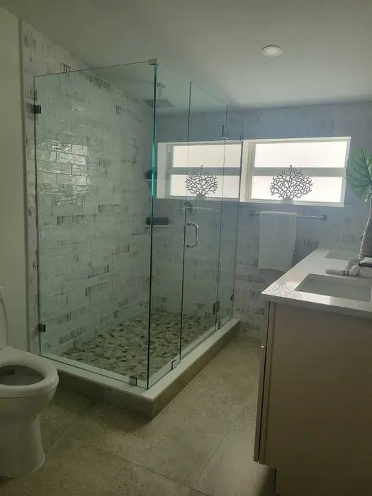 Finished master bathroom with geometric tile shower enclosure, white vanity with dual sink, marble-effect wall tiles, and frosted glass windows with decorative patterns
