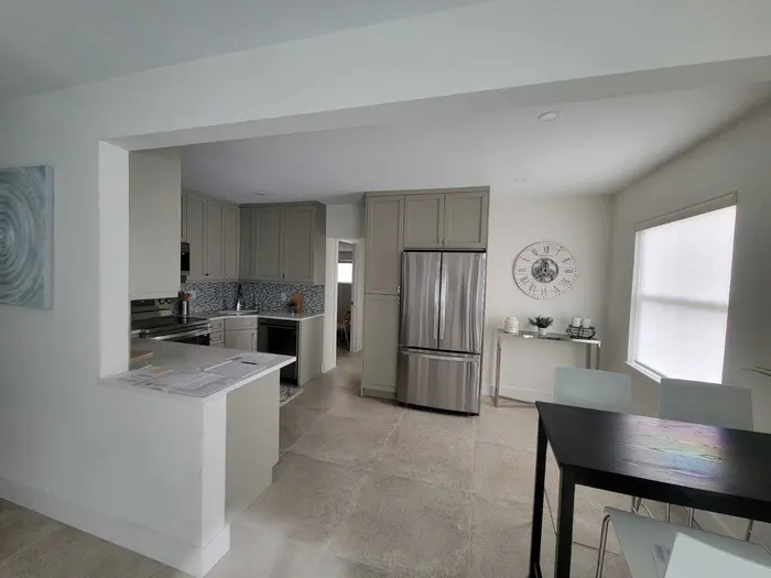 Completed modern kitchen with gray cabinetry, stainless steel appliances, mosaic backsplash, white drywall, and polished concrete flooring