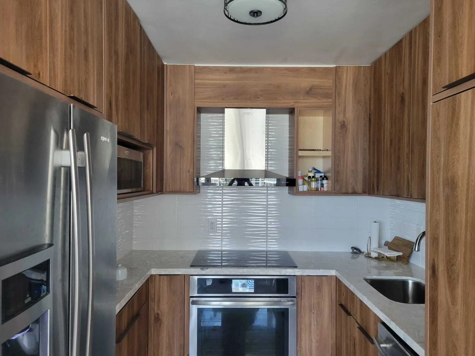 Completed modern kitchen with warm wood cabinetry, white subway tile backsplash, stainless steel appliances, granite countertops, and island with cooktop