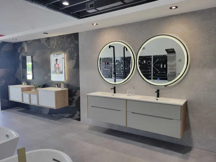 Exposición de baño moderno con dos tocadores, espejos redondos iluminados y accesorios contemporáneos en una tienda al por menor