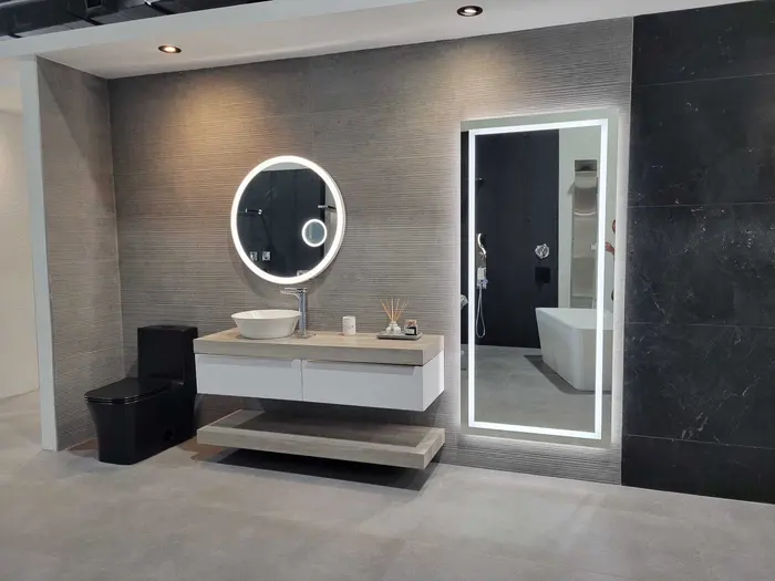 Exhibición de baño moderno con vanidad de lavabo blanco, espejo LED, inodoro negro, bañera blanca independiente, paredes con azulejos grises texturizados y azulejos negros de acento