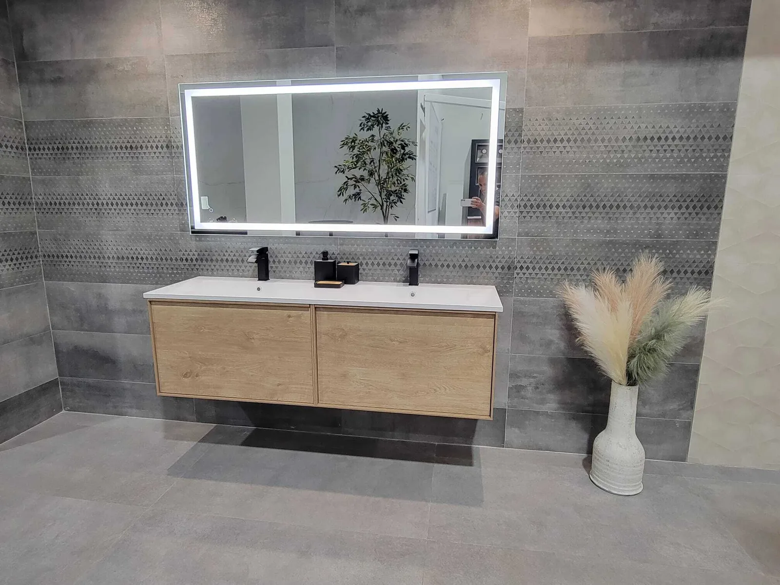 Baño completado moderno con mueble flotante de madera natural, lavabo doble blanco, espejo iluminado LED, paredes de azulejo gris con franja geométrica decorativa y accesorios