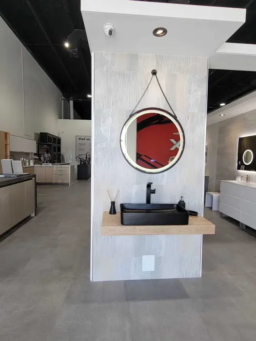 Exposición de vanidales de baño que muestra un moderno lavamanos negro sobre una repisa de madera con espejo LED redondo y grifo negro, parte de una exhibición más grande de accesorios de baño.