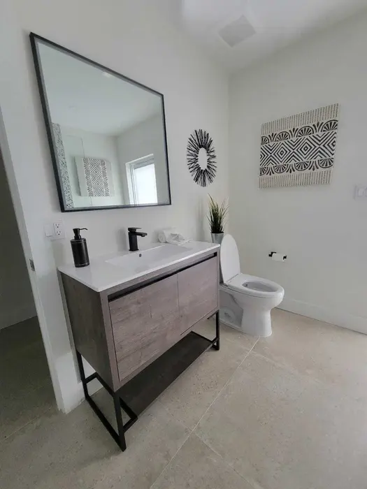 Baño moderno terminado con tocador flotante de madera, encimera de cuarzo blanco, espejo contemporáneo con marco negro, inodoro blanco y arte mural geométrico en paredes blancas limpias