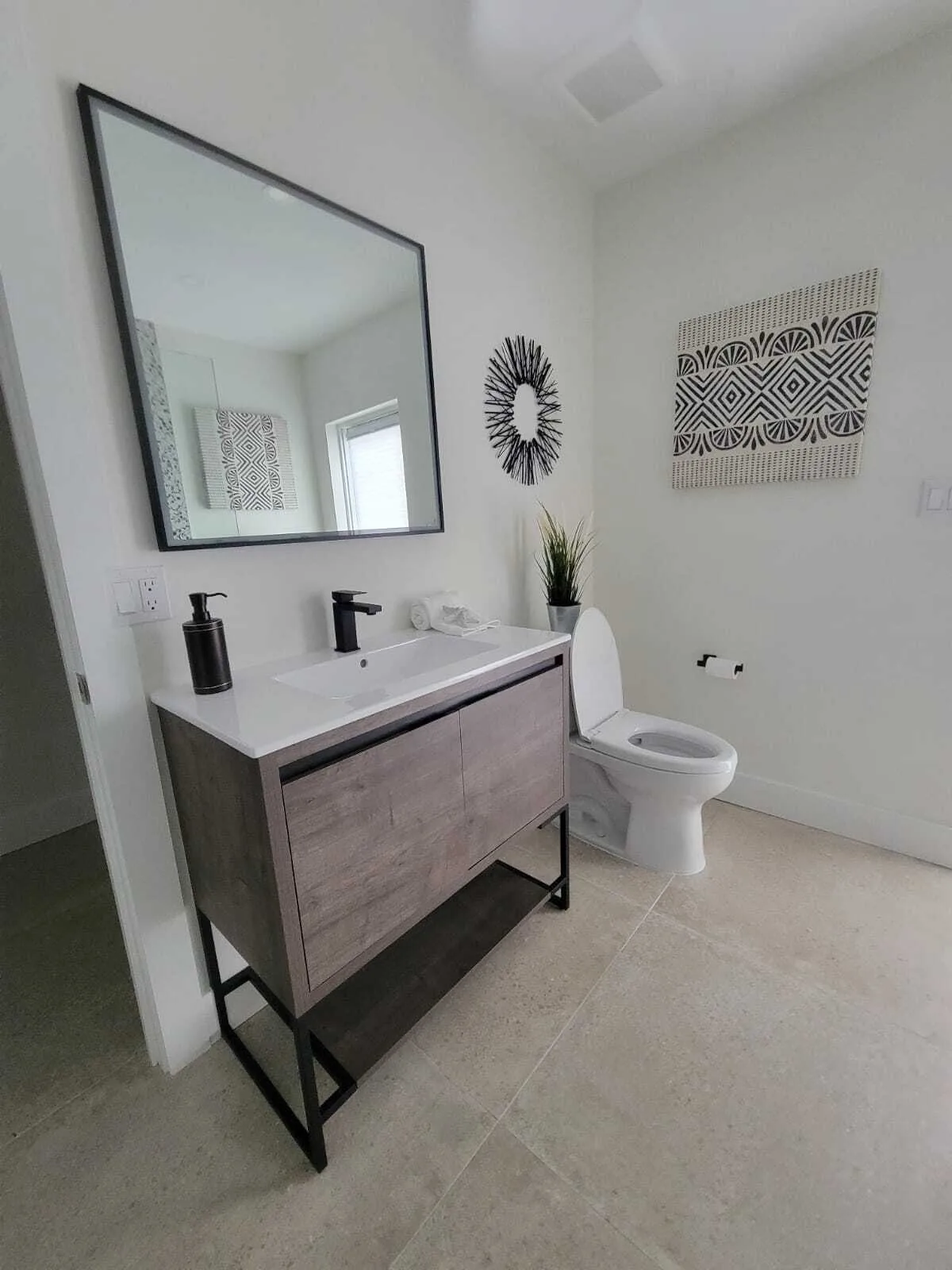 Baño moderno terminado con tocador flotante de madera, encimera de cuarzo blanco, espejo contemporáneo con marco negro, inodoro blanco y arte mural geométrico en paredes blancas limpias