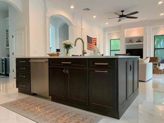 Cocina moderna completada con gabinetes oscuros, isla con encimera en cascada, iluminación colgante y espacio de vida abierto