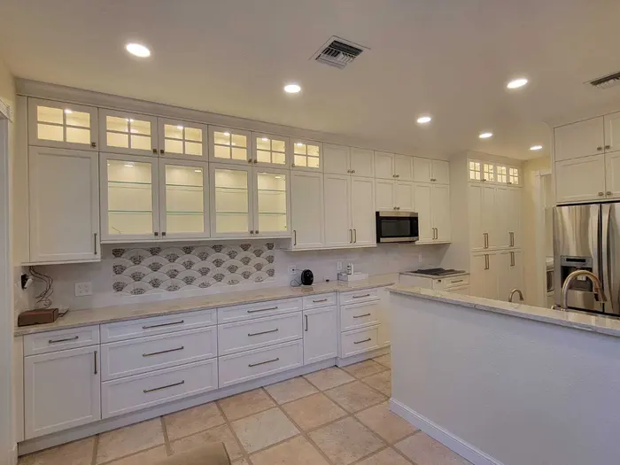 Remodelación de cocina completada con gabinetes pintados de blanco, azulejos decorativos en el salpicadero, electrodomésticos de acero inoxidable, encimeras de cuarzo e iluminación empotrada