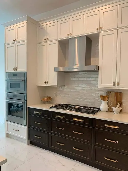 Cocina moderna con gabinetes bicolor: frentes superiores en crema y inferiores en negro, campana extractora de acero inoxidable, estufa de gas, azulejos tipo metro en salpicadero y encimeras de mármol con electrodomésticos integrados.