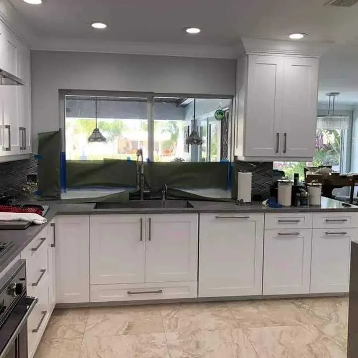 Cocina moderna completada con gabinetes pintados en blanco, encimeras negras, piso de azulejos de mármol, puertas corredizas de cristal grandes con vistas al jardín e iluminación empotrada en el techo