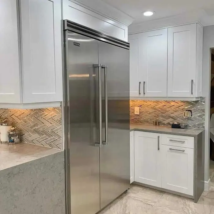 Cocina moderna con gabinetes pintados de blanco, salpicadero con patrón espiga efecto madera, refrigerador Viking acero inoxidable, y encimeras de cuarzo gris en remodelación residencial completada.