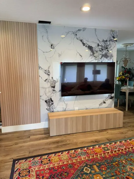 Sala de estar moderna con pared de acento de mármol, paneles de pared con textura de madera, iluminación empotrada, consola flotante con televisor montado en pared y piso de madera