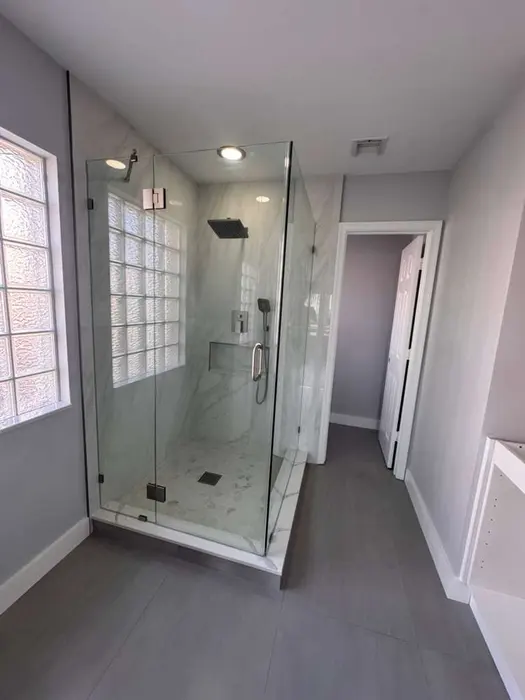Baño de lujo completado con cabina de ducha con azulejos de mármol, puertas de vidrio sin marco, piso de azulejo oscuro y ventana de bloques de vidrio personalizados