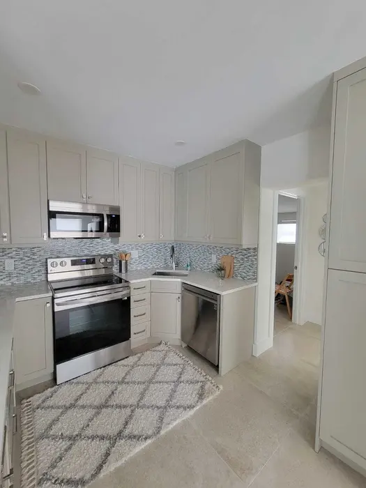 Cocina recién remodelada con gabinetes shaker color crema, salpicadero de azulejos de vidrio mosaico, electrodomésticos de acero inoxidable, encimeras de granito y piso de azulejo pulido en una casa residencial