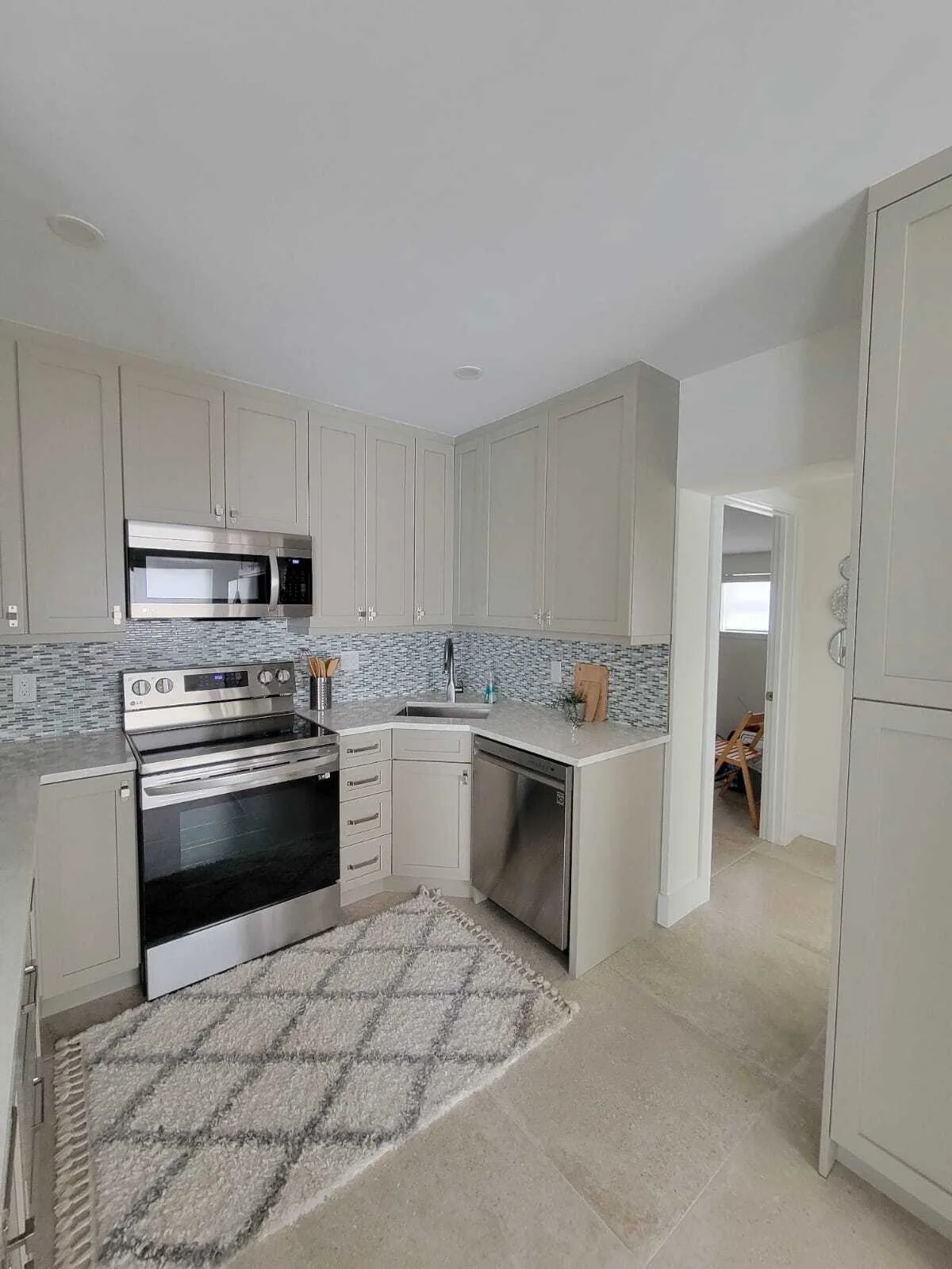 Cocina recién remodelada con gabinetes shaker color crema, salpicadero de azulejos de vidrio mosaico, electrodomésticos de acero inoxidable, encimeras de granito y piso de azulejo pulido en una casa residencial
